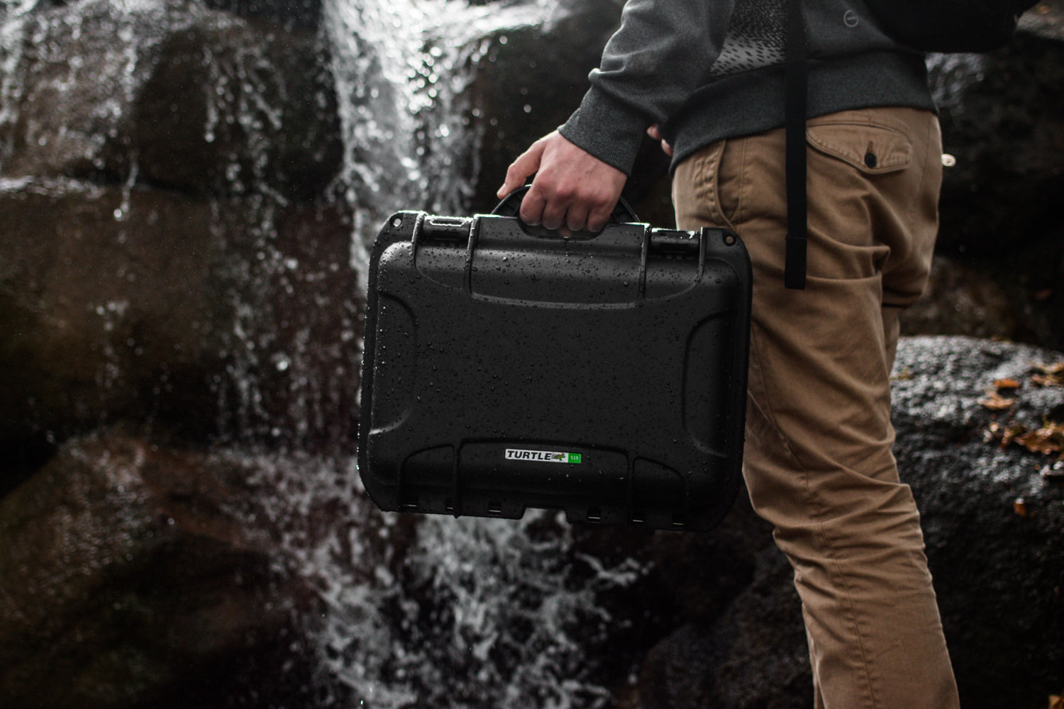 man holding equipment case in front of waterfall